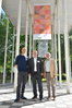 Bürgermeister und zwei Künstler stehen unter einer Fahne der Ausstellung