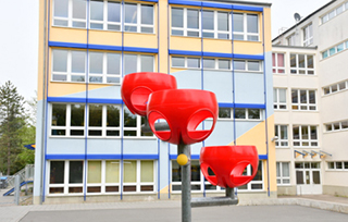 Schulgebäude vom Schulhof aus mit rotem Spielgerät im Vordergrund