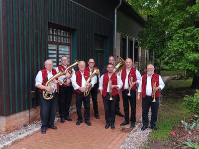 Mehrere Musiker der Orlishäuser Dorfmusikanten stehen mit Blasinstrumenten auf einem Weg vor einem Gebäude und posieren gemeinsam für ein Gruppenfoto im Grünen.