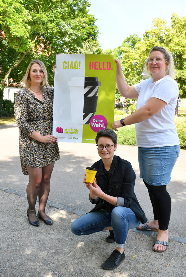 Lena Kob vom Stadtmarketing, Beatrice Fischer, stellvertretende Leiterin der Stadt- und Kreisbibliothek, sowie Stephanie Schieritz, Nachhaltigkeitsbeauftragte bei der Bäckerei Bergmann zeigen ein Plakat der Kampagne Mission Mehrweg