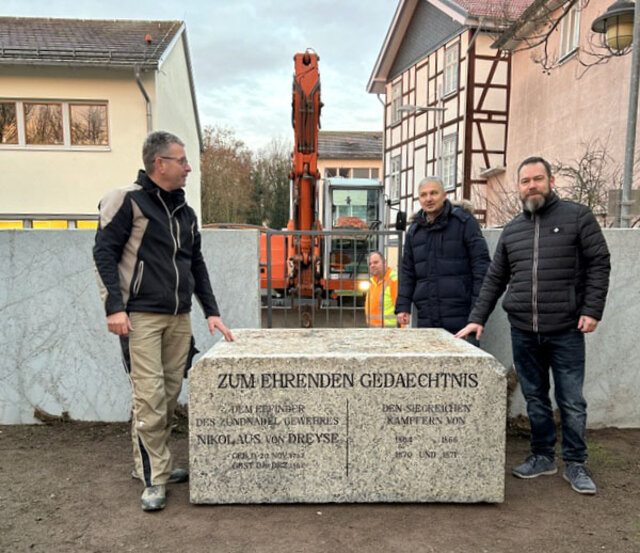 Marco Bösemann, Dr. Hans-Diether Dörfler, Museumsleiter und Beisitzer im Sömmerdaer Heimat- und Geschichtsverein, sowie Maik Mirre, Vorstandsmitglied vom Schützenverein „Nicolaus von Dreyse (v. l.). Der Sockel steht auf der Erde. Links und rechts davon stehen insgesamt drei Männer: Marco Bösemann von der Firma Bösemann, Dr. Hans-Diether Dörfler, Leiter Museum und Archiv sowie Beisitzer im Heimat- und geschichtsverein, sowie Maik Mirre vom Vorstand des Schützenvereins. Im Hinter steht hinter dem Zaun ein Kran. Vor dem Kran schaut ein Mitarbeiter des Betriebshofes in Richtung Kamera.