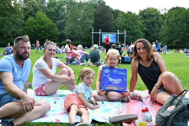 Eine Familie sitzt im Sömmerdaer Stadtpark auf einer Picknickdecke und schauen in die Kamera. Hinter ihnen befindet sich eine große Leinwand, auf der ein Film gezeigt wird.