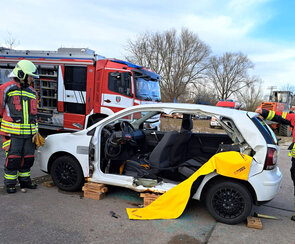Ein Feuerwehrmann steht an einem weißen Auto, bei dem die zwei Türen auf der Fahrerseite herausgeschnitten wurden.
