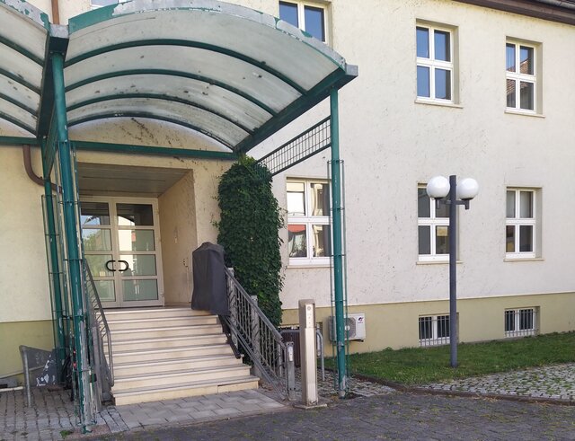 Hintereingang des Verwaltungsgebäudes Poststraße 1 in Sömmerda Überdachter Hintereingang des Verwaltungsgebäudes Poststraße 1 in Sömmerda mit einer Treppe, seitlichem Geländer und verglaster Eingangstür. An diesem Zugang entsteht ab September 2026 ein barrierefreier Zugang.