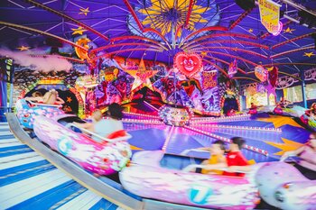 Ein bunt beleuchtetes Fahrgeschäft auf einem Jahrmarkt mit schnell fahrenden Wagen und leuchtenden Dekorationen. Das Bild vermittelt Tempo, Spaß und die lebhafte Atmosphäre eines Volksfestes.
