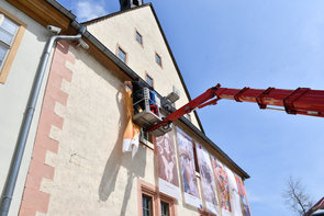 Auf der Plattform einer Hebebühne stehend bringen zwei Männer die großen Fahnen an der Rathausfassade an.