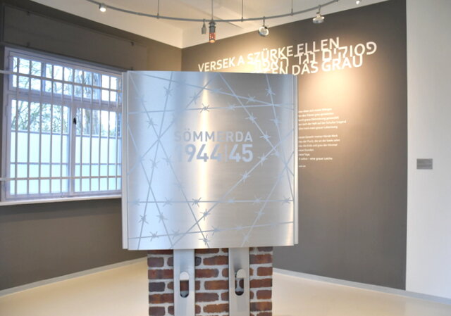 Der Gedenk- und Bildungsort "Tor 8". Im Torhaus 8 steht im Zentrum ein Edelstahlkubus. Die zur Eingangstür gerichtete Seite zeigt stilisiertes Stacheldraht sowie den Schriftzug Sömmerda 1944/1945. An der rechten Wand ist ein Gedicht einer der Häftlingsfrauen zu lesen.