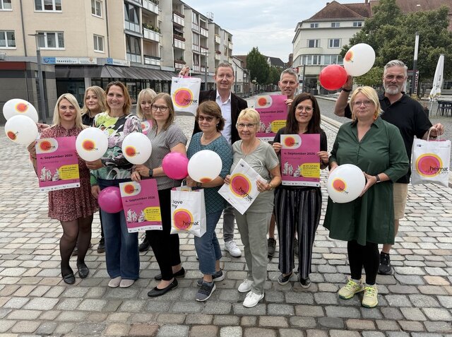 Akteure und Organisatoren des Heimatshoppens 2026 mit Werbemitteln für den Aktionstag. Teilnehme Geschäftsleute und Organisatoren des Heimatshoppens stehen in zwei Reihen hintereineander. In den Händen halten sie Luftballons, Plakate und Einkaustüten aus Papier, mit denen für das Heimatshoppen geworben werden soll. Im Hintergrund zeigt sich eine der Einkaufsstraßen in der Sömmerdaer Innenstadt.
