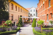 Blick in den Historischen Rosengarten am Dreyse-Haus in Sömmerda mit Blumenbeeten, Sitzplätzen und Gebäuden im Innenhof.