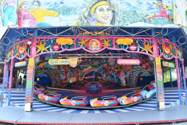 Ein größeres Fahrgeschäft auf dem Frühlingsfest. Es handelt sich um eine Art Karussell für Erwachsene. Links stehen außerhalb des Fahrgeschäftes einige Leute.