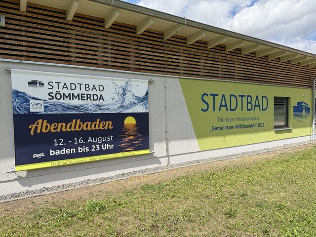 An der Frontseite des Empfangsgebäudes im Stadtbad hängt ein großes Plakat. Auf diesem steht unter anderem das Datum, an dem das Abendbaden angeboten wird. Zudem wird auf die verlängerte Öffnungszeit bis 23:00 Uhr an den Tagen des Abendbadens hingewiesen.