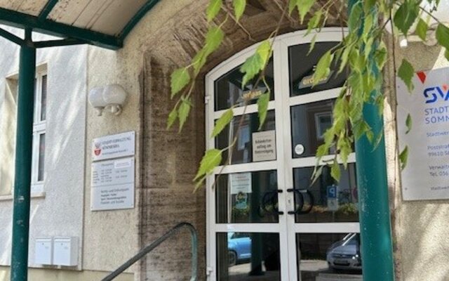 Eingang eines Gewerbeamts mit Glasdoppeltür, Schildern und Überdachung, daneben ein Schild der Stadtverwaltung