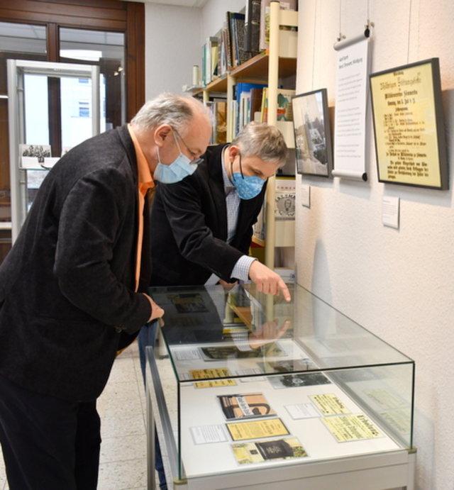 Bürgermeister und Leiter des Archivs blicken in eine der Ausstellungsvitrinen.
