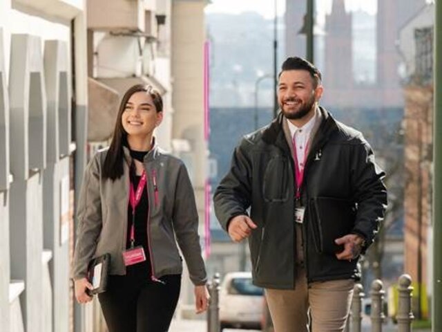Beratungsgespräche zum Glasfaserausbau Zwei Mitarbeitende der Telekom gehen mit Ausweisen um den Hals durch eine Straße und sind im Rahmen der Beratung zum Glasfaserausbau unterwegs.