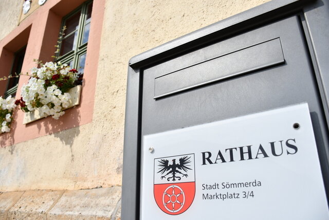 Ein Ausschnitt der Fassade des Rathauses mit Blumenkästen n Fenstern und dem Briefkasten in Edelstahl-Ausführung. Daran ist ein Schild mit dem Stadtwappen von Sömmerda und den Wörtern Rathaus Stadt Sömmerda, Marktplatz 3/4 angebracht.