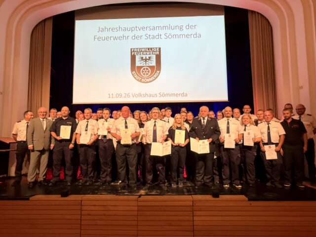 Gruppenfoto mit den geehrten, beförderten und ausgezeichnenten Feuerwehrleuten. Die beförderten, berufenen und geehrten Feuerwehrleute stehen mit ihren Urkunden in den Händen in drei Reihen hintereinander gemeinsam mit Bürgermeister, Stadtbrandinspektor sowie Kreisbrandmeister auf der Bühne.