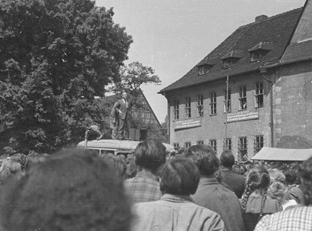 Eine am Sömmerdaer Rathaus versammelte Menschenmenge hört einem Mann zu, der von einem Autodach herab zu ihr spricht. Foto vom 17. Juni 1953 in Sömmerda. Quelle: Stadtarchiv Sömmerda, Historisches Fotoarchiv, Nr. 04699.