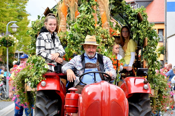 Ein Bauer sitz auf einem festlich geschmückten roten Traktor. Neben ihm sitzt ein Mädchen. Sie fahren bei dem Sömmerdaer Ernteumzug mit.