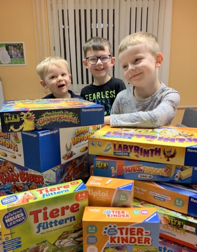 Kindergarten-Kinder schauen hinter zu zwei Türmen aufgebauten Spielen hervor.