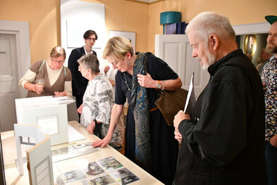 Gäste der Gedenkveranstaltung schauen sich den den mit dem ersten Preis versehenen Gestaltungsentwurf an. Rechts im Bild steht mit Wolfgang Schneider eines der Mitglieder der Künstlergruppe, die den Siegerentwurf gestaltet hat.  