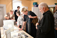 Gäste der Gedenkveranstaltung schauen sich den den mit dem ersten Preis versehenen Gestaltungsentwurf an. Rechts im Bild steht mit Wolfgang Schneider eines der Mitglieder der Künstlergruppe, die den Siegerentwurf gestaltet hat.  