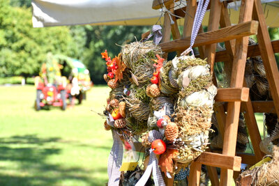 Impression vom Bauernmarkt. Auf der Rastenfläche im Stadtpark steht ein Holzgestell, an dem herbstliche Kränze hängen. In Hintergrund steht eine der Kutschen, die am Ernteumzug teilgenommen haben.