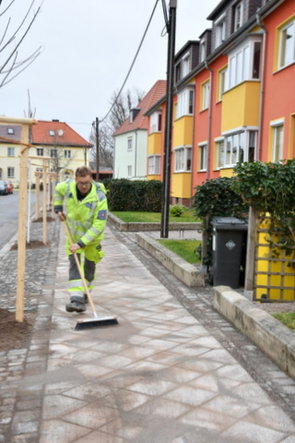 Sand wird in die Fugen des reparierten Fußweges eingekehrt.