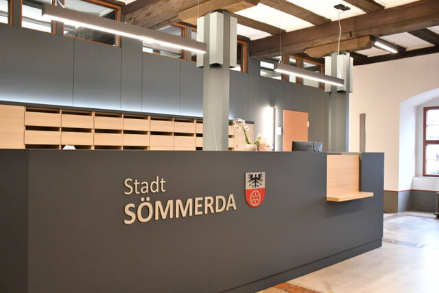 Das Rathaus-Foyer mit Empfangstresen. Das Foyer des Rathauses mit dem Empfangstresen. An der Vorderseite sind der Schriftzug Stadt Sömmerda sowie das Stadtwappen angebracht. Hinter dem Empfangstresen sitzt eine Person.