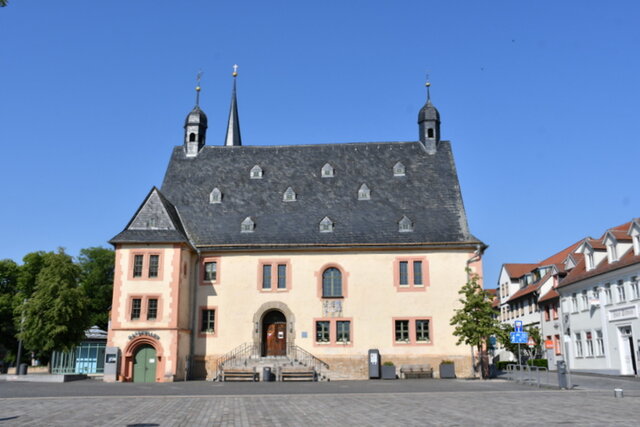 Das Rathaus von Sömmerda von vorn gesehen bei blauem Himmel und sonnigem Wetter. An der rechten Ecke steht ein kleinerer Baum. Rechts am Rathaus vorbei blickt man auf eine Häuserzeile. Linkerhand vom Rathaus ist ein Teil des Obermarktes mit mehreren Bäumen zu sehen. Vor dem Rathaus befindet sich eine größere gepflasterte Fläche, die zum Marktplatz gehört.