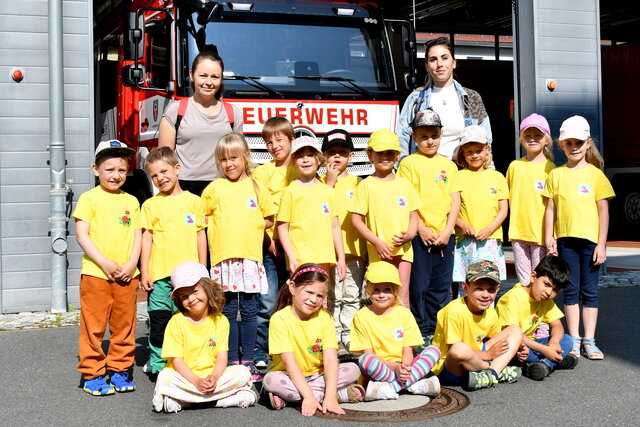 Eine Gruppe von rund 15 Kindern in gelben T-Shirts posiert gemeinsam mit zwei Erzieherinnen vor einem roten Feuerwehrfahrzeug. Die Kinder lachen und sitzen oder stehen fröhlich vor dem Fahrzeug. Das Bild wurde im Rahmen des Zuckertütenfests 2025 auf der Feuerwache Sömmerda aufgenommen.