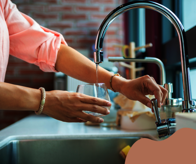 Eine Frau betätigt den Wasserhahn in der Küche und füllt ein Glas mit Leitungswasser