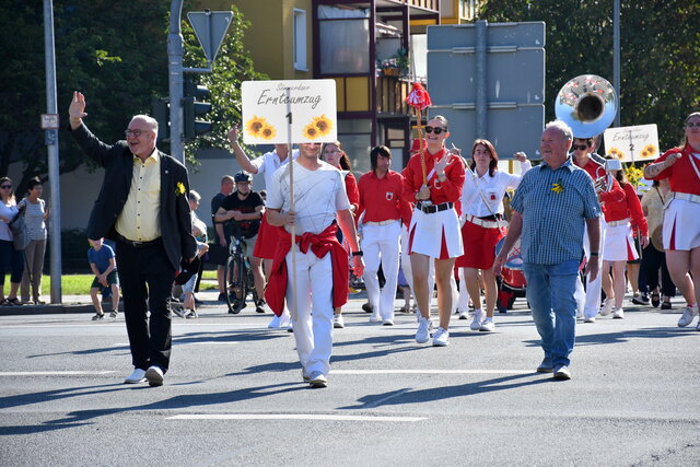 Bürgermeister Ralf Hauboldt winkt den Zuschauern des Ernteumzugs zu. Neben ihm steht ein läuft ein junger Mann mit einen Schild der ersten Teilnehmer