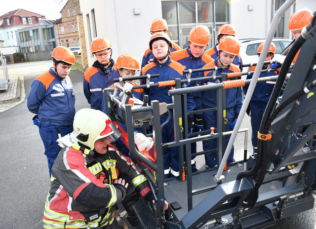 Mitglieder der Jugendfeuerwehr stehen am Personentransportkorb einer Drehleiter, an der der Ausbilder technische Details erklärt.