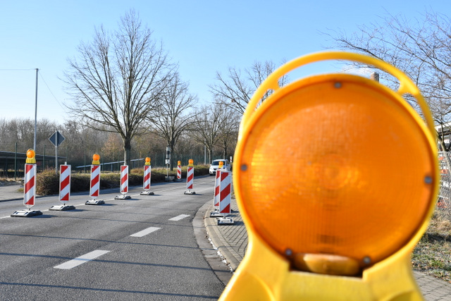 Mit orangfarbener Warnleuchte und rot-weiß-gestreifte Sicherheitsbaken ist der Straßenbereich, auf dem der Fußgängerüberweg gebaut werden soll, abgesperrt.