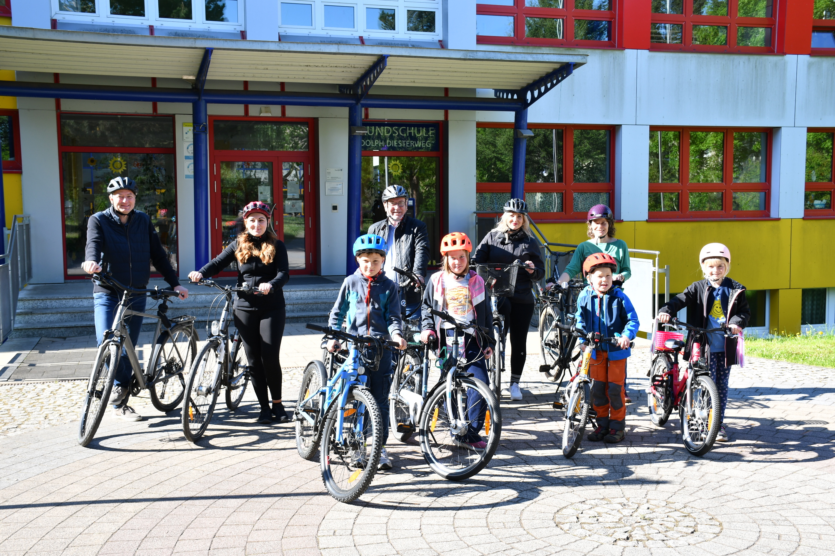 Personengruppe aus Kindern und Erwachsenen mit Fahrrädern vor dem Eingang der Diesterweg-Grundschule in Sömmerda, bereit zum Start des STADTRADELN 2025. Alle tragen Fahrradhelme, im Hintergrund ist das bunte Schulgebäude zu sehen.