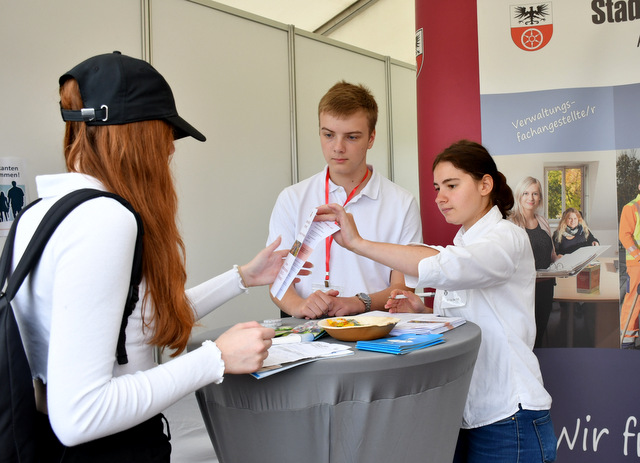 Zwei Auszubildende der Stadtverwaltung zeigen am Stand der Stadtverwaltung auf der BIB einer Schülerin einen Flyer mit Informationen zu Ausbildungsmöglichkeiten.