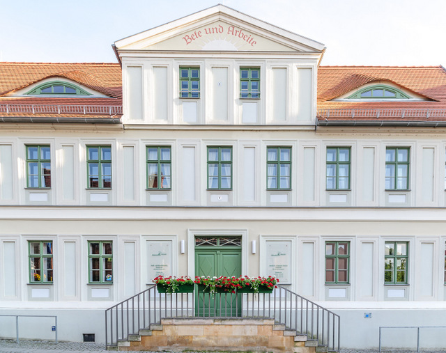 Die Vorderansicht des Dreyse-Hauses mit dem beidseitigen Treppenaufgang sowie den transparenten Schildern mit dem Hinweis auf die Öffnungszeiten sowie die Kontaktmöglichkeiten von Bibliothek und Museum links und rechts neben der Eingangstür.