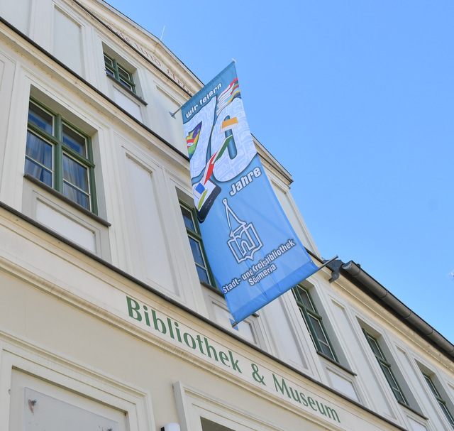 Am Gebäude des Dreysehauses mit Bibliothek und Museum weht eine Flagge, auf der auf blauem Hintergrund ein bunter Bücherstapel sowie in Weiß die Wortgruppe 70 Jahre gedruckt sind. Desweiteren steht ebenfalls in Weiß Stadt- und Kreisbibliothek sowie das Logo der Bibliothek auf dem senkrechten Banner geschrieben.