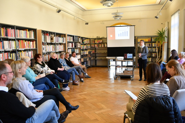 Eine Frau erläutert vor Beamer und Leinwand stehend den Bibliotheksentwicklungsplan. Die Teilnehmerinnen und Teilnehmer der Veranstaltung sitzen auf Stühlen in einem offenen Kreis vor ihr im Saal der Sömmerdaer Bibliothek.