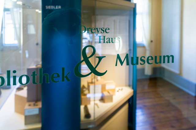 Eine Glastür im Dreyse-Haus mit der Aufschrift Bibliothek und Museum, dahinter eine Ausstellung.t 