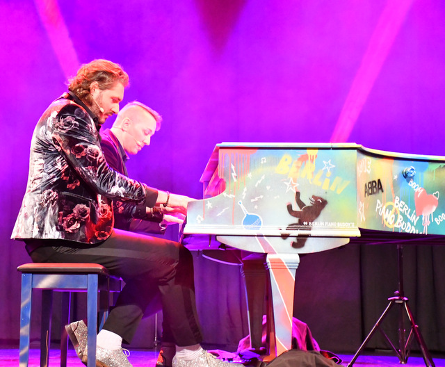zwei Männer sitzen auf der Bühne an einem farbig bunt gestalteten Klavier und spielen vierhändig.