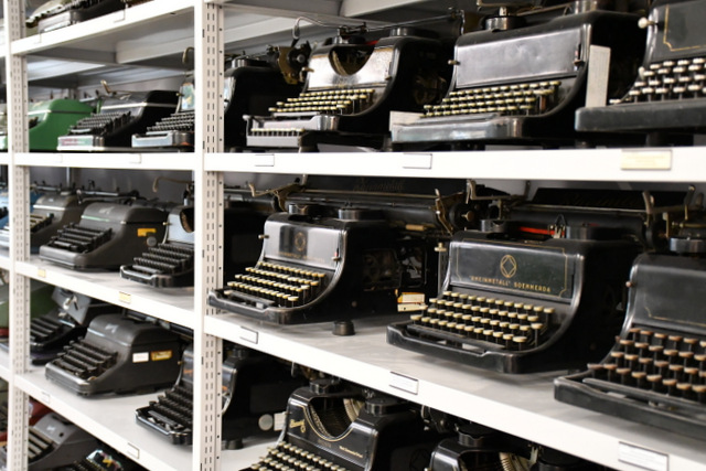 In einem Metallregal stehen Schreibmaschinen aus der Produktion von Rheinmetall und des späteren Büromaschinenwerks.