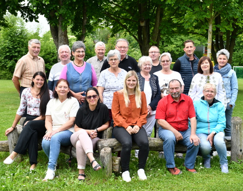 Mitglieder des Seniorenbeirates und die Ansprechpartnerin der Stadtverwaltung für den Seniorenbeirat stehen (hintere Reihe) bzw. sitzen (vordere Reihe) im Grünen auf dem Gelände des Bürgerzentrums im Stadtteil Neue Zeit/Offenhain. Im Hintergrund stehen etliche große Bäume.