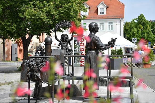 Blick durch Blumen auf die Bronzeskulpturengruppe auf dem Obermarkt in Sömmerda.