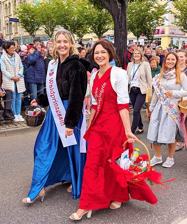 Sömmerdas Waidprinzessin in einem blaue Kleid mit dunkelblauem Jäckchen und weißer Schärpe mit der Aufschrift Waidprinzessin und die Thüringer Erdbeerkönigin in langem roten Kleid und mit Körbchen in der Hand laufen im Umzug beim Thüringentag in Gotha. Am Straßenrand stehen viele Zuschauer. Foto: Steffen Töppe