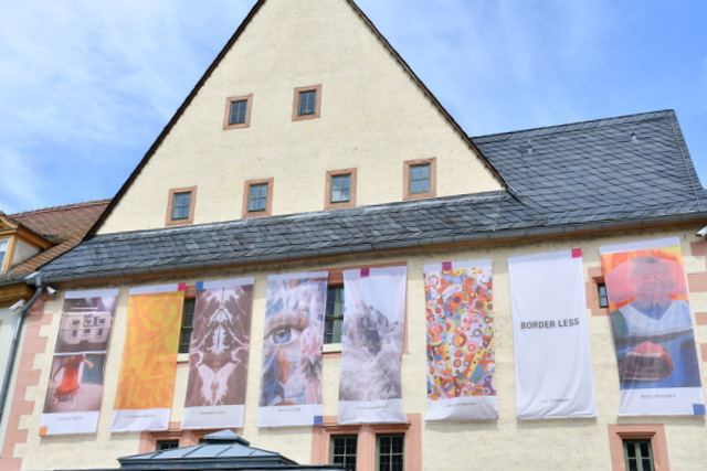 Acht große Fahnen mit aufgedruckten Fotografien, Malerei und Grafik hängen an der Rathaus-Fassade.