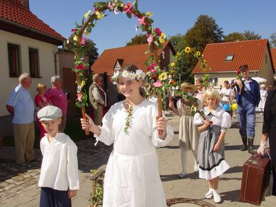 Festlich angezogene Kinder mit Blumenbögen in den Händen sind beim Umzug dabei.