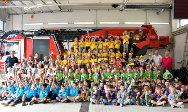 Die Kindergartenkinder sitzen oder stehen für das Abschlussfoto vor dem Fahrzeug mit der Drehleiter.